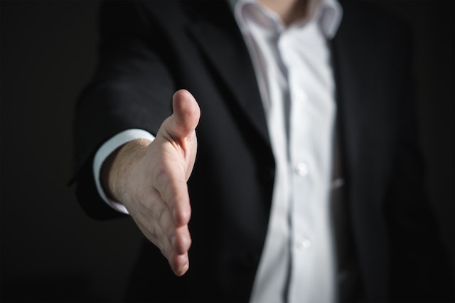 person in dark suit reaching out their hand for a handshake